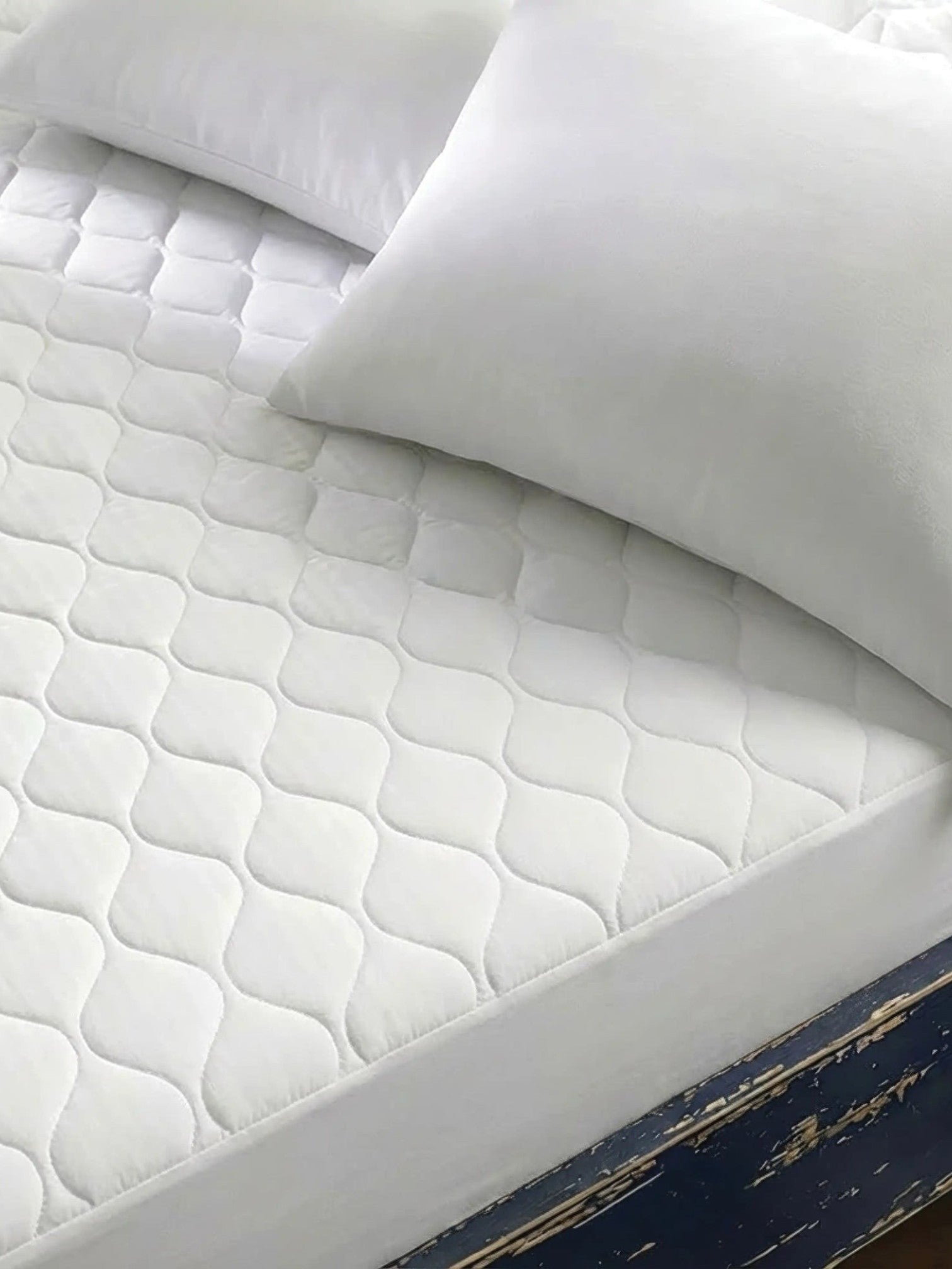 Valiant Products white quilted mattress pad with ogee pattern on a bed with pillows